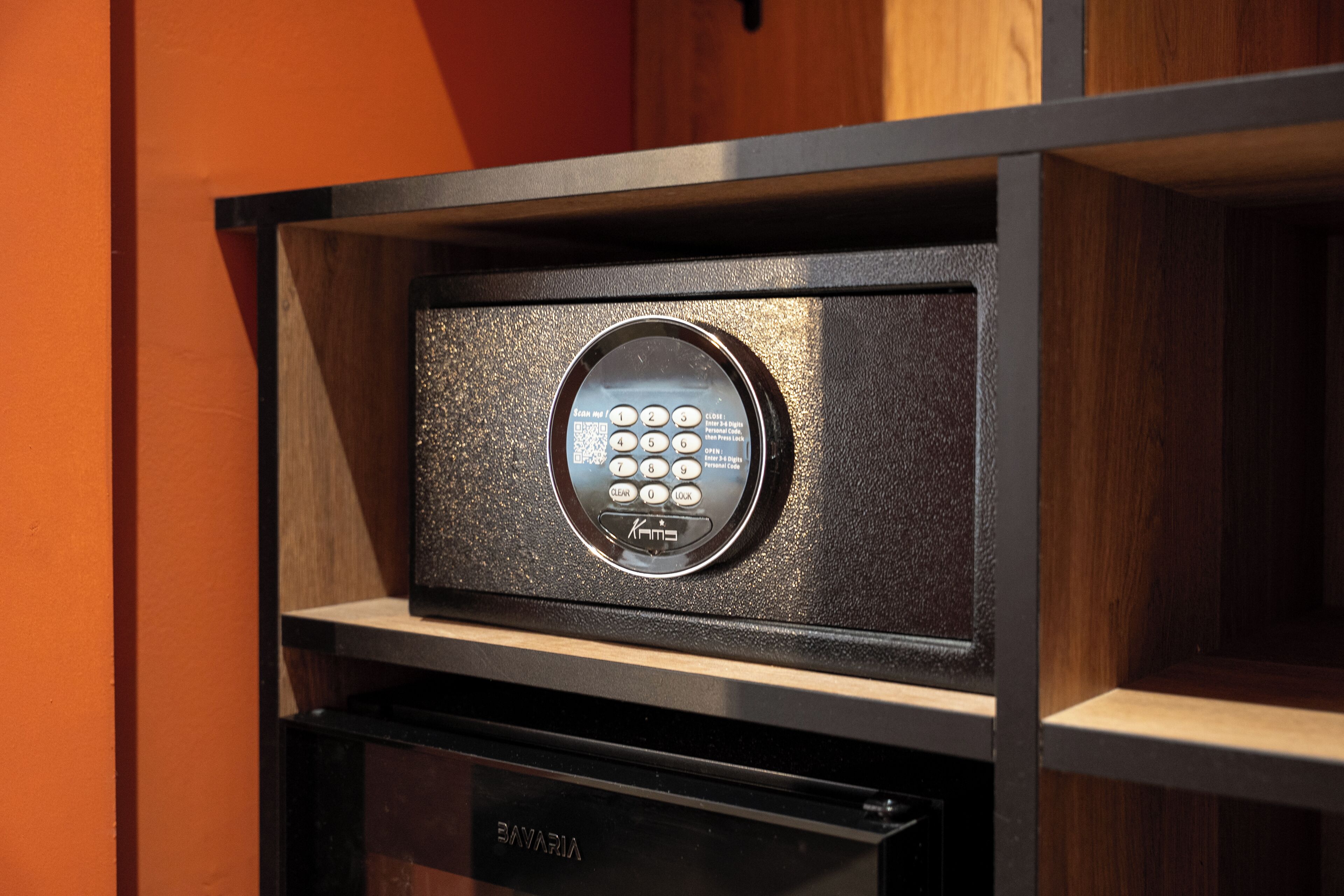 A keypad lock on a wooden shelf with a black electronic device below it.