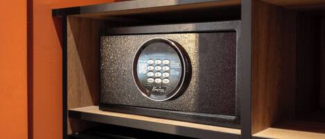 A keypad lock on a wooden shelf with a black electronic device below it.