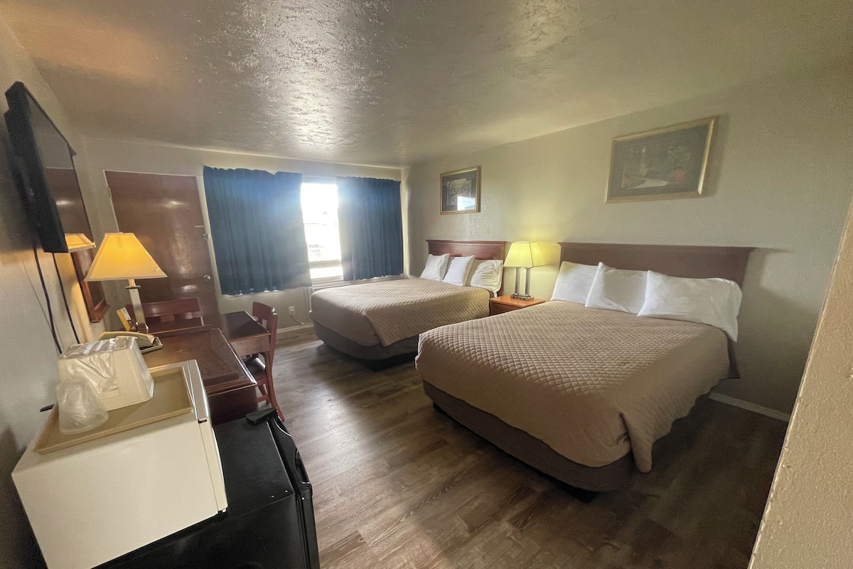 A hotel room with two beds, a desk, a chair, a dresser, and a mirror.