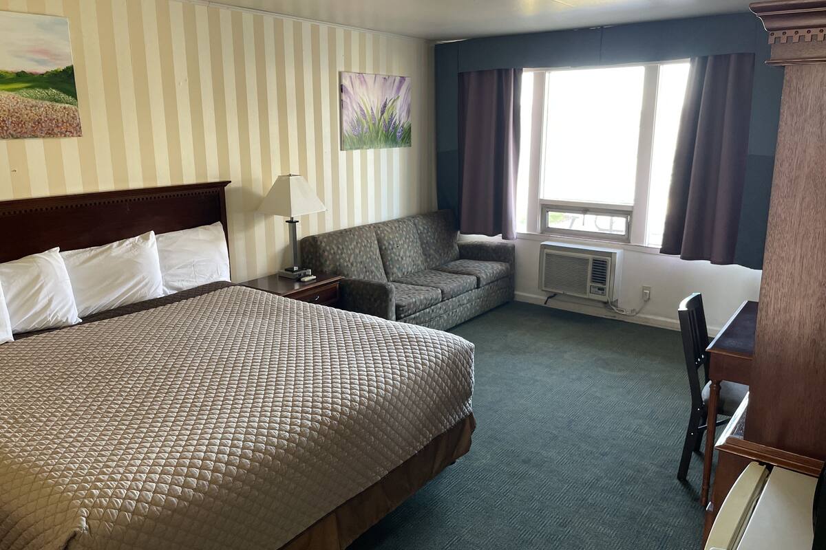 A hotel room with a large bed, a sofa, a desk, and a window with curtains.