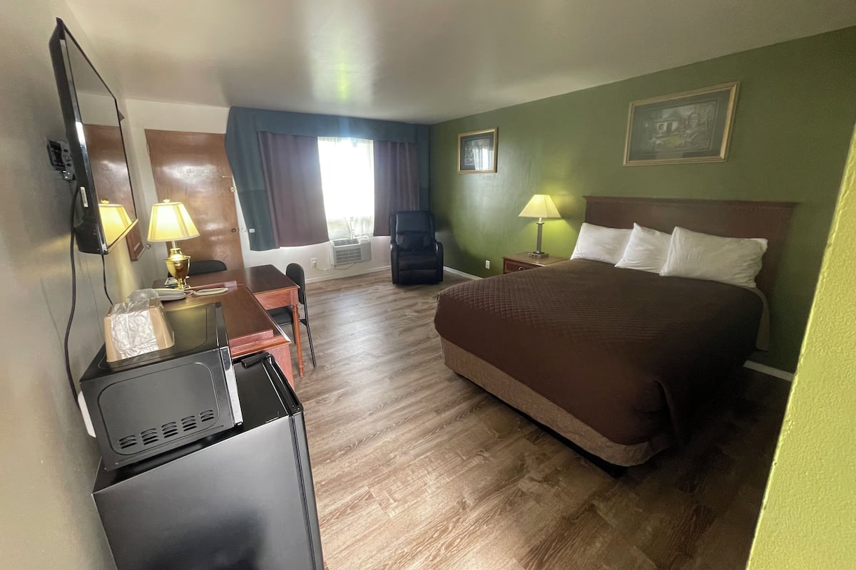 A hotel room with a bed, desk, chair, TV, and lamps.