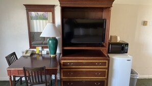 A hotel room with a wooden desk, a television, a lamp, a microwave, and a trash bin. - Motel Oasis (Moses Lake)