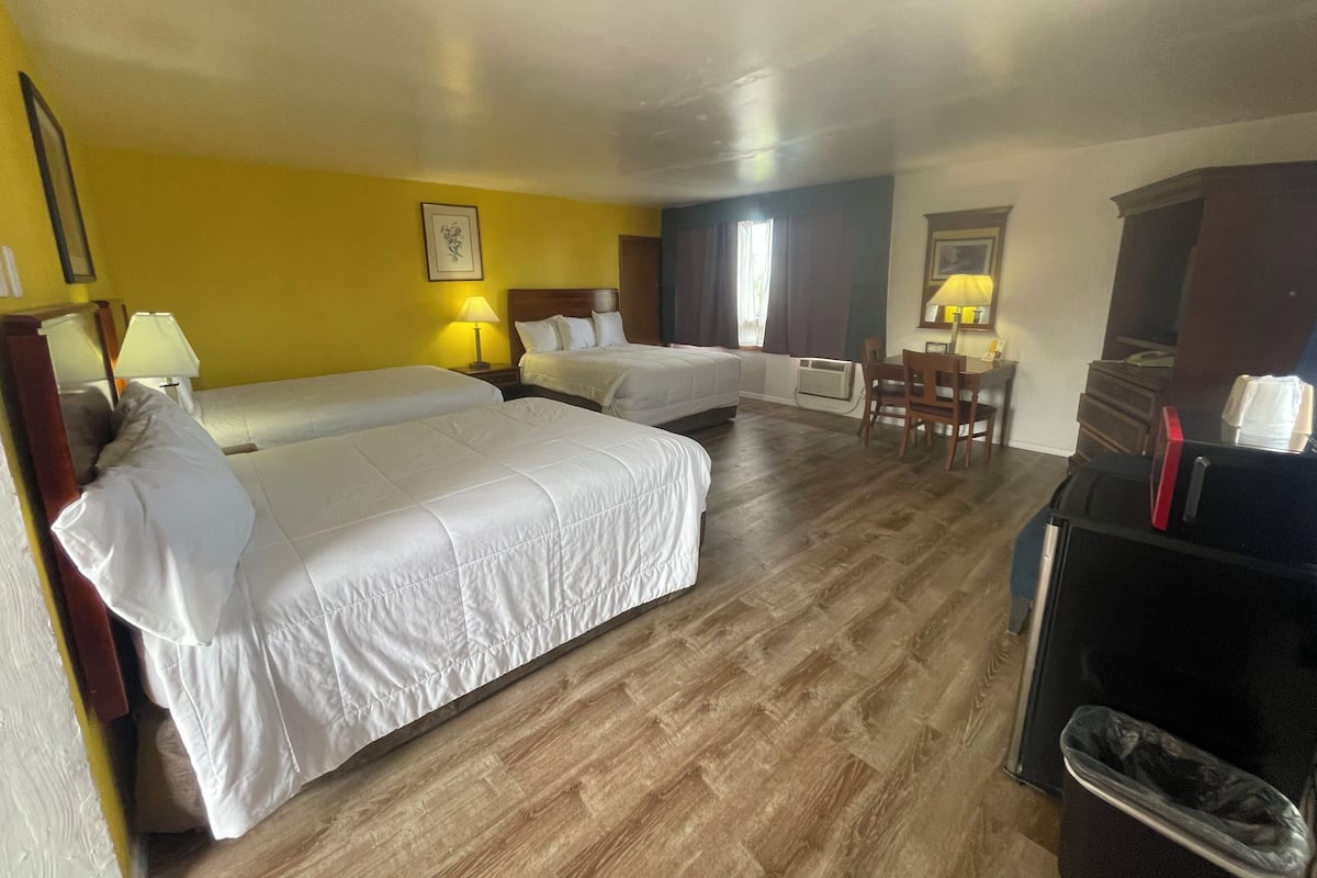 A hotel room with two beds, a desk, a chair, and a dresser.