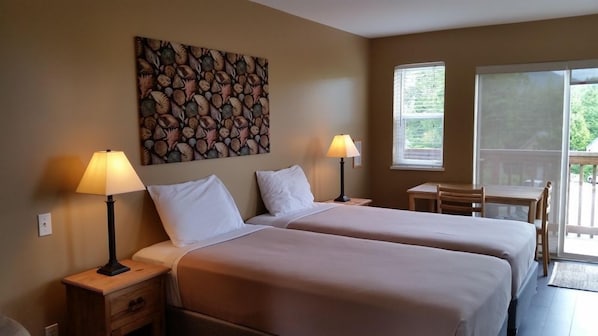 A hotel room with two beds, a painting on the wall, a desk, and a balcony with a view.