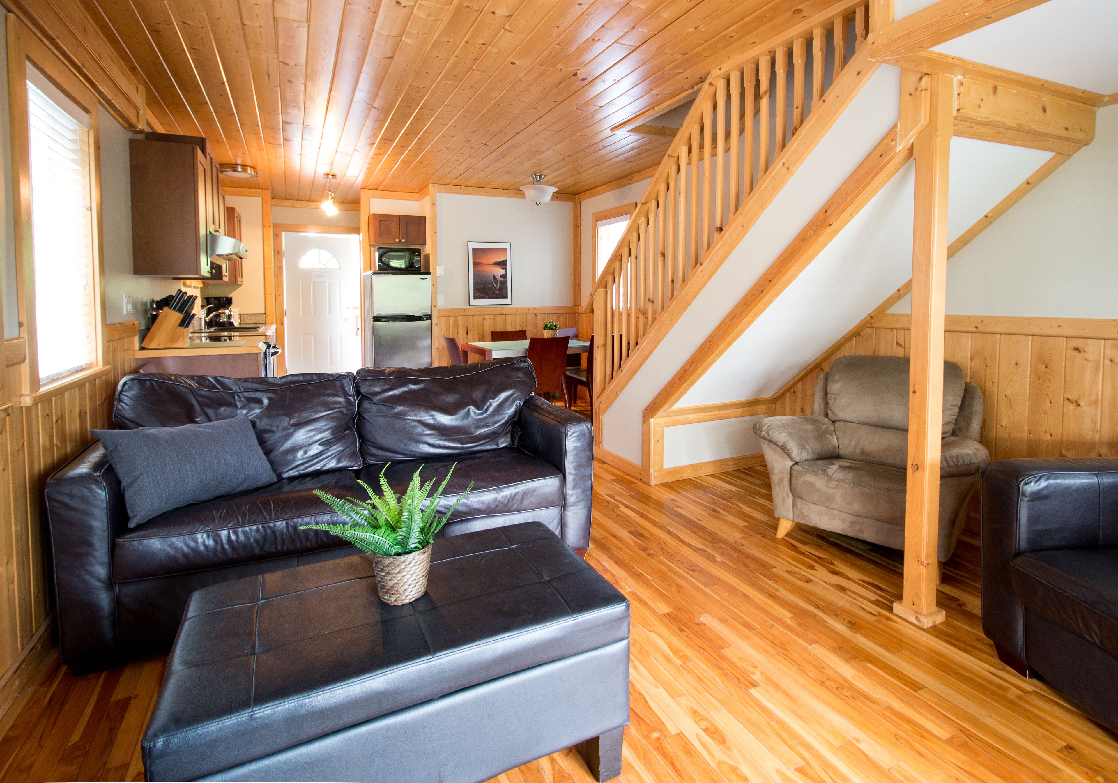 Un intérieur de chalet chaleureux avec un escalier en bois, des canapés en cuir et un coin repas.