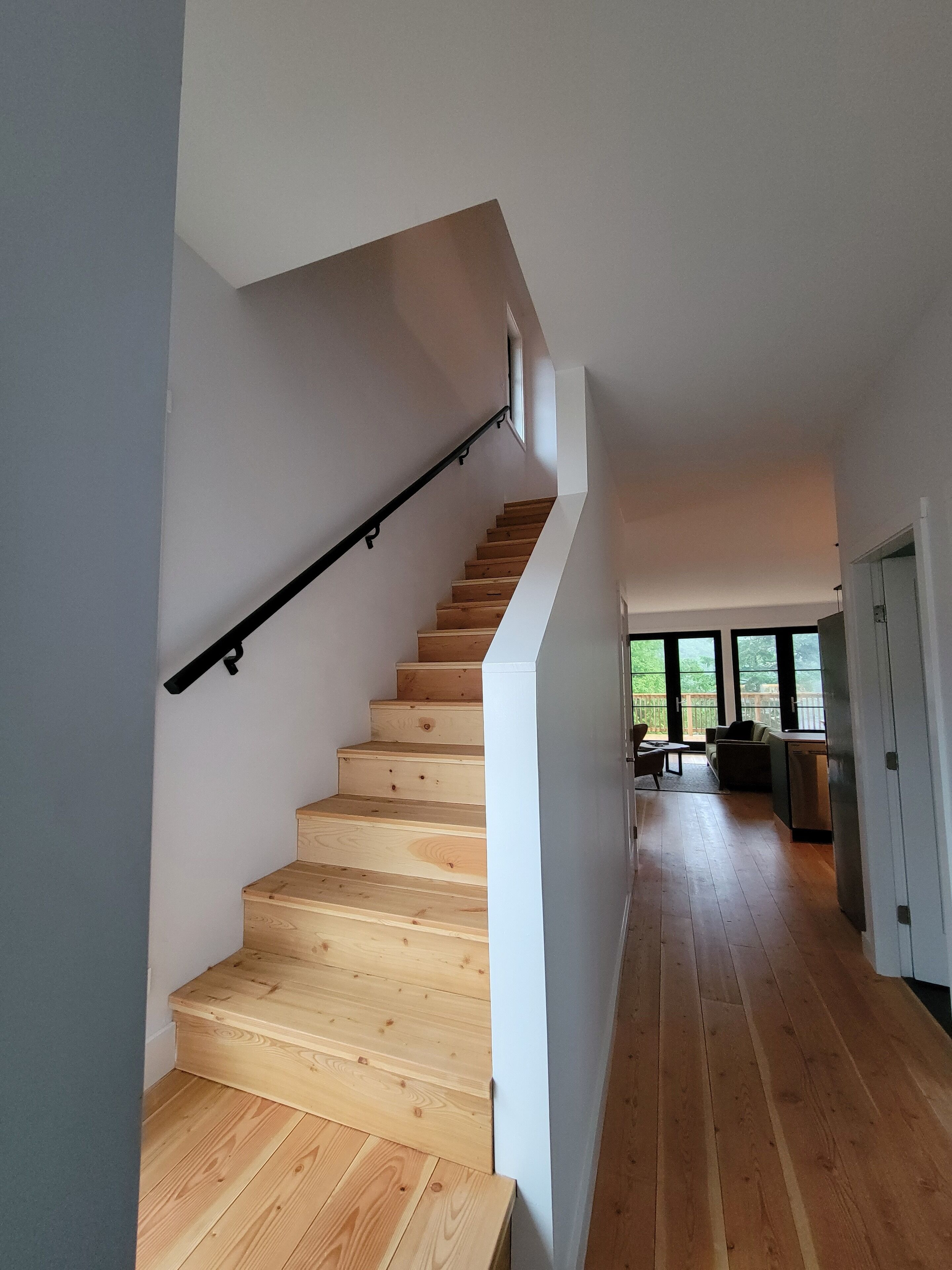 Ein modernes Interieur mit einer Holztreppe, einer Küchenzeile und Blick durch große Fenster.