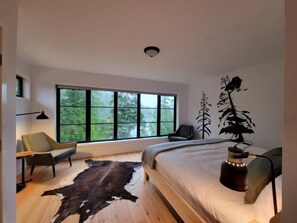 Quarto moderno com uma grande janela, uma cama, uma cadeira, uma escrivaninha e um tapete de couro de vaca.