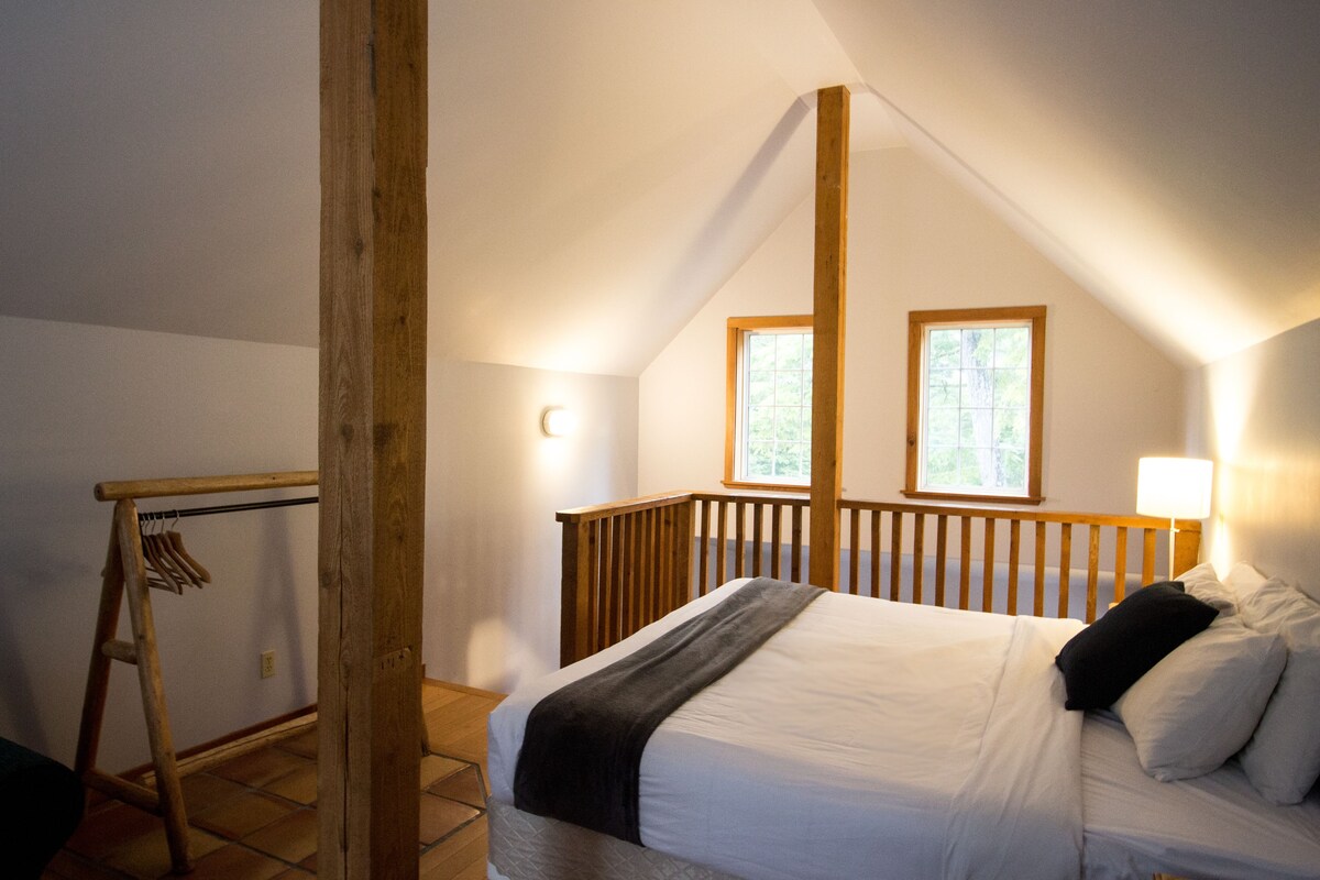 Quarto com estrutura de cama de madeira, cabeceira, janela e luminária.