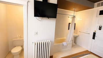 Une salle de bain comprenant des toilettes, un radiateur, une douche avec une porte en verre et une baignoire.