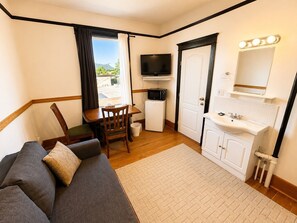 A compact room with a sofa, a dining table, a TV, a microwave, a sink, and a window with curtains. - Richca Heritage Hotel (Chilliwack)