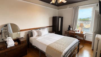 Quarto de hotel com cama, escrivaninha, guarda-roupa, espelho e janela com vista.