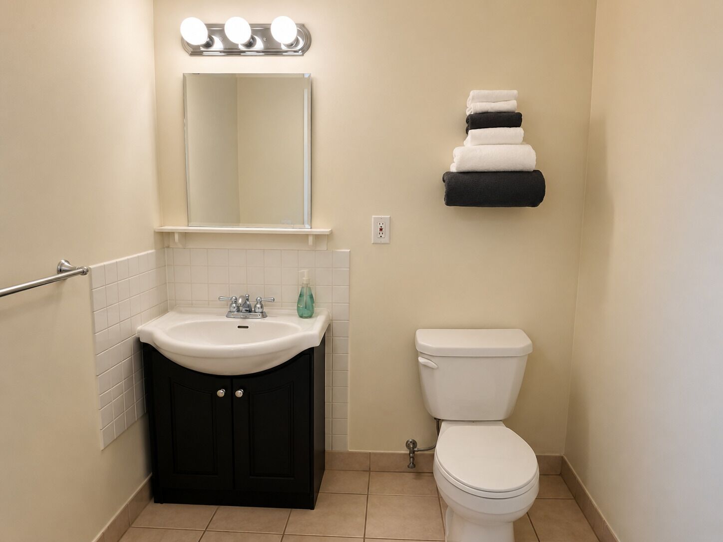 Une salle de bain avec un lavabo blanc, des meubles noirs, des toilettes blanches et un miroir avec des lumières au-dessus.