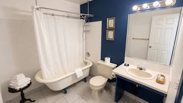 A bathroom with a bathtub, toilet, sink, and a mirror with lights.