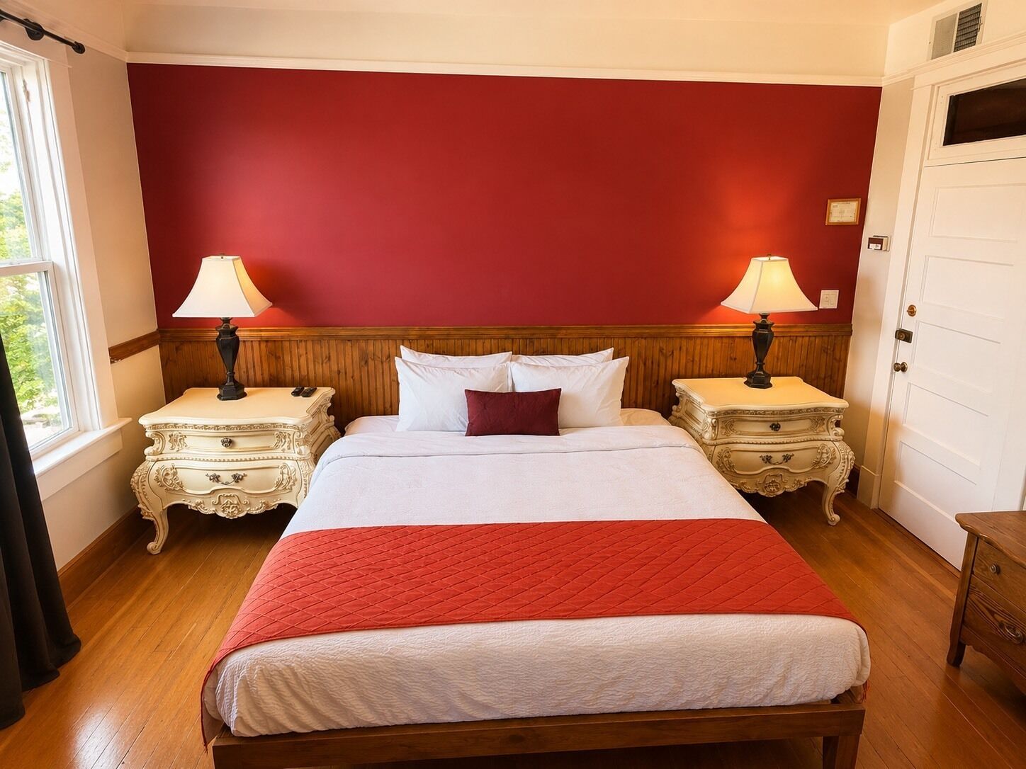A hotel room with a large bed, two bedside tables with lamps, a wooden headboard, and a red accent wall.