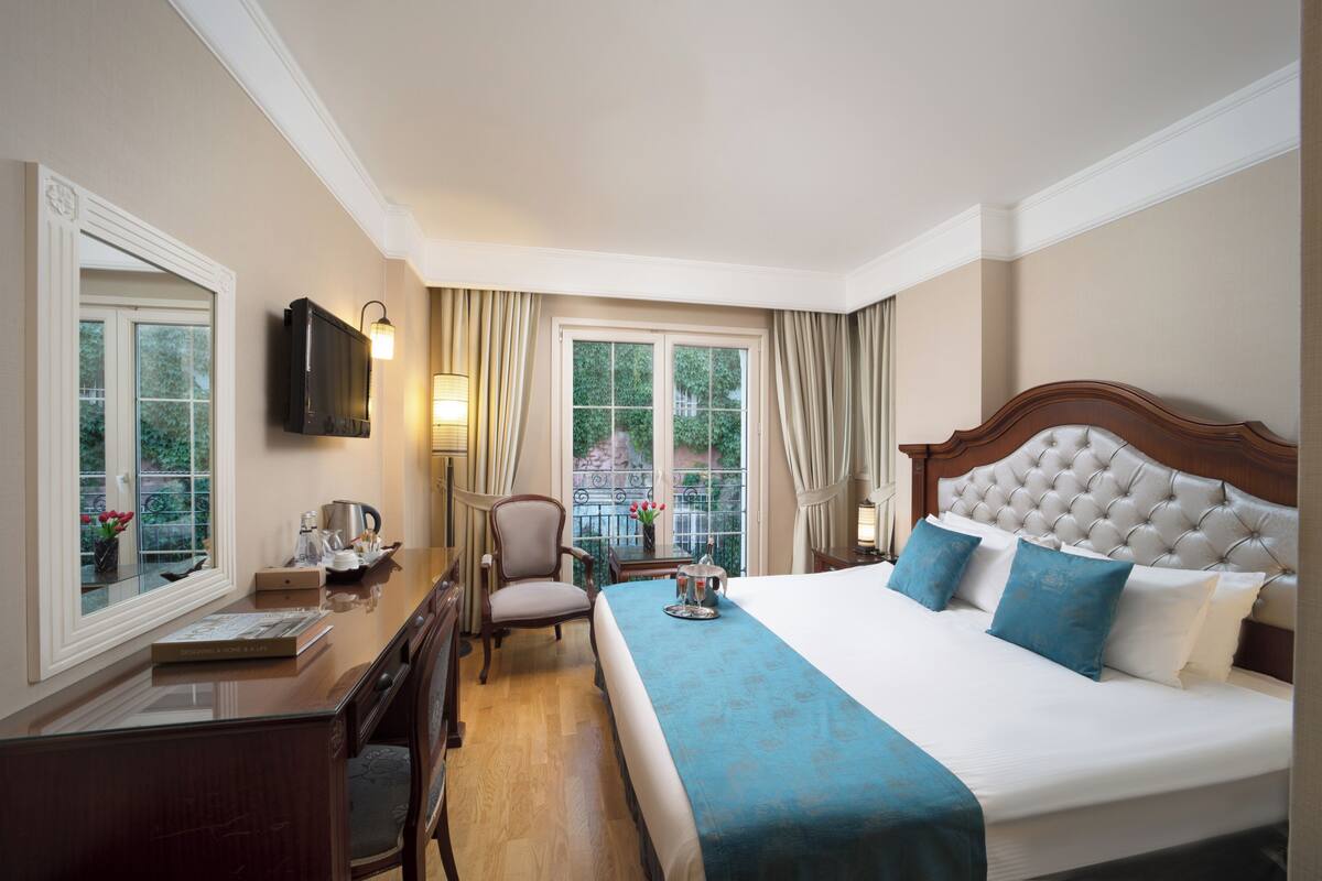Une chambre d’hôtel avec un grand lit, un bureau avec une chaise, une télévision et une fenêtre avec des rideaux.
