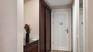 A hallway with a wooden cabinet, a vase with dried flowers, and a white door with a doorbell.
