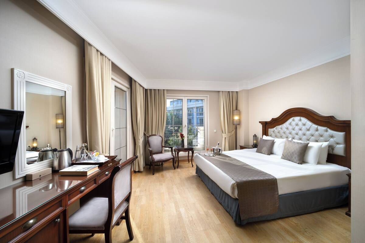 Une chambre d’hôtel avec un grand lit, un bureau, une chaise, une télévision et une fenêtre avec des rideaux.