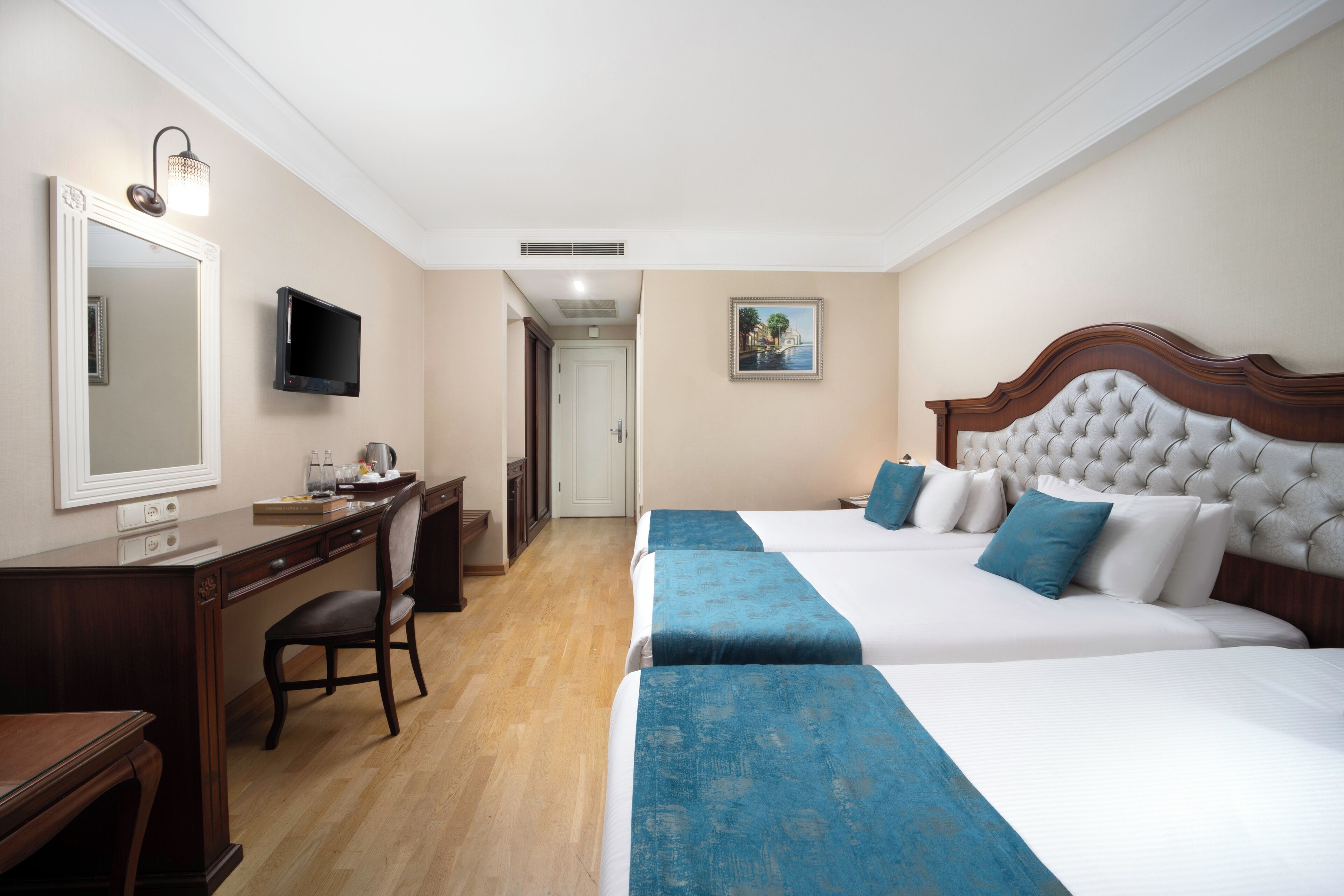 Habitación de hotel con dos camas, un escritorio, una silla, un televisor y un cuadro en la pared.