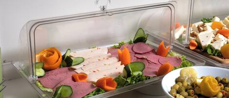 A buffet with various food items including meats, vegetables, and a bowl of olives.