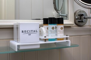 Un estante de baño con una caja etiquetada como "RECITAL" y tres botellas de colores distintos.