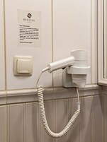 Camera d'albergo con asciugacapelli montato a parete, porta asciugamani e cartello sulla conservazione degli asciugamani.