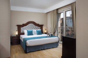Una habitación de hotel con una cama grande, una mesita de noche, una lámpara y un ventanal con cortinas.
