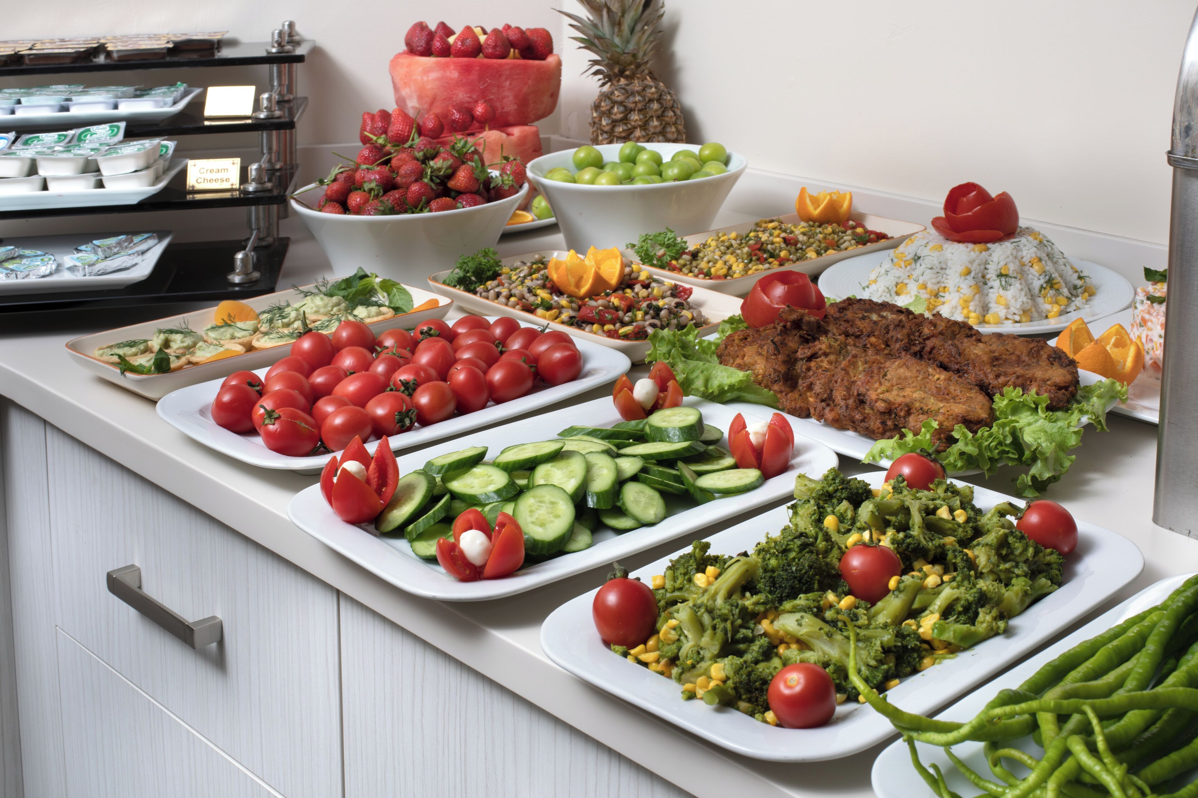 A buffet with various dishes including tomatoes, cucumbers, broccoli, and meat.