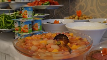 Un bufé con distintos alimentos, entre ellos frutas, verduras y salsas.