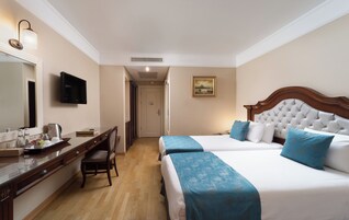 A hotel room with two beds, a desk with a chair, a television, and a painting on the wall.