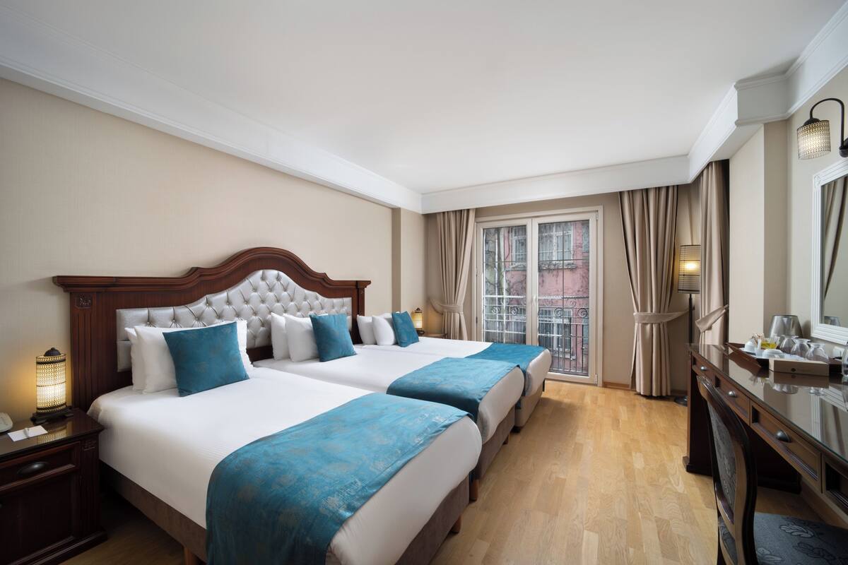 Une chambre d’hôtel avec deux lits, un bureau et une fenêtre avec des rideaux.
