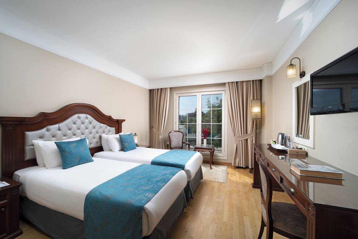 Une chambre d’hôtel avec deux lits, un bureau, une chaise, une télévision et une fenêtre avec des rideaux.