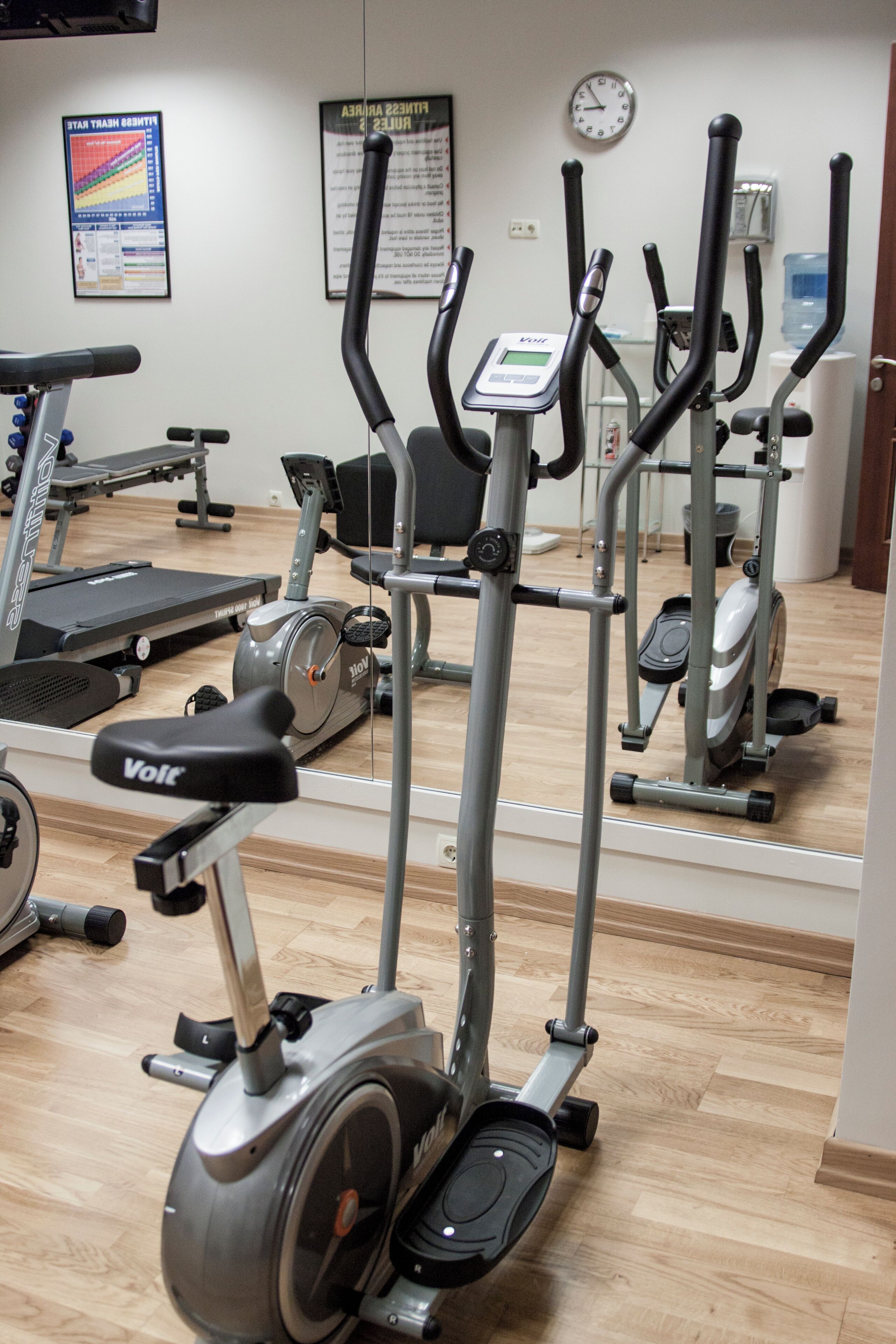 Un gimnasio con bicicletas estáticas, cintas de correr y un reloj de pared.