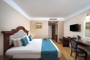 Camera d'albergo con un letto grande, una scrivania, una sedia, una televisione e un quadro appeso al muro.