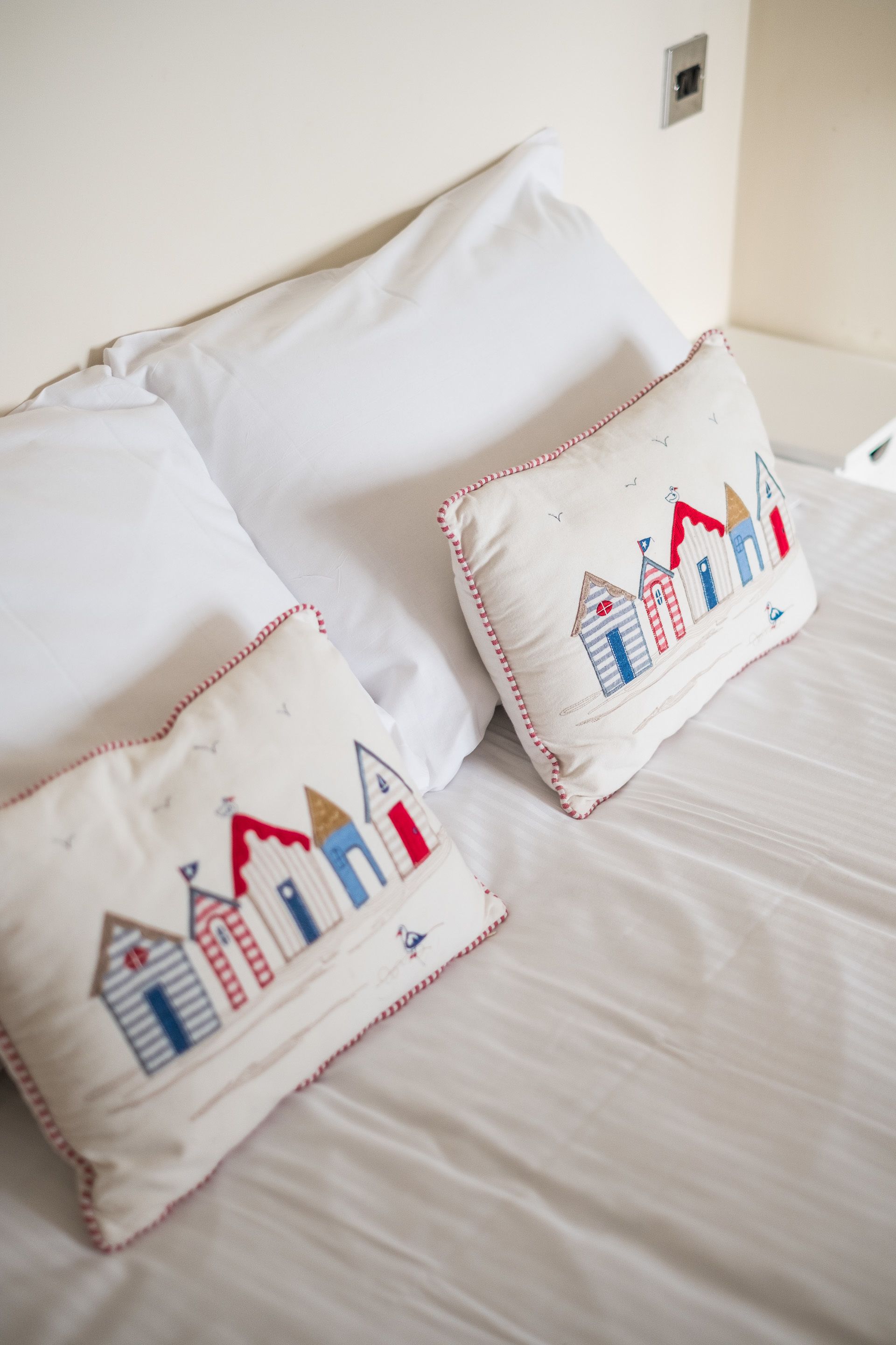 A bed with white bedding and two decorative pillows featuring a nautical theme.