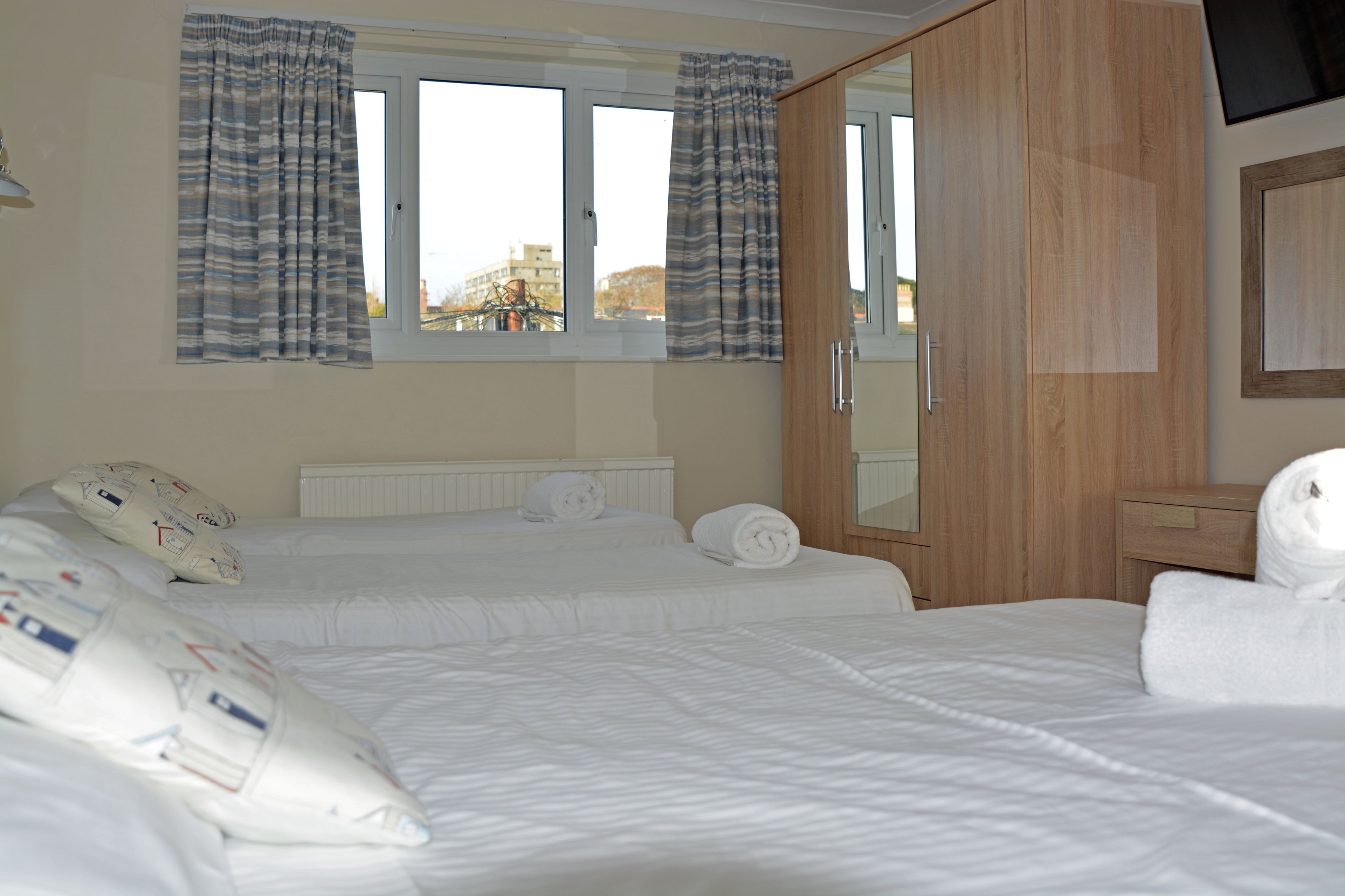 Habitación de hotel con dos camas, un armario de madera, un espejo y una ventana con cortinas.