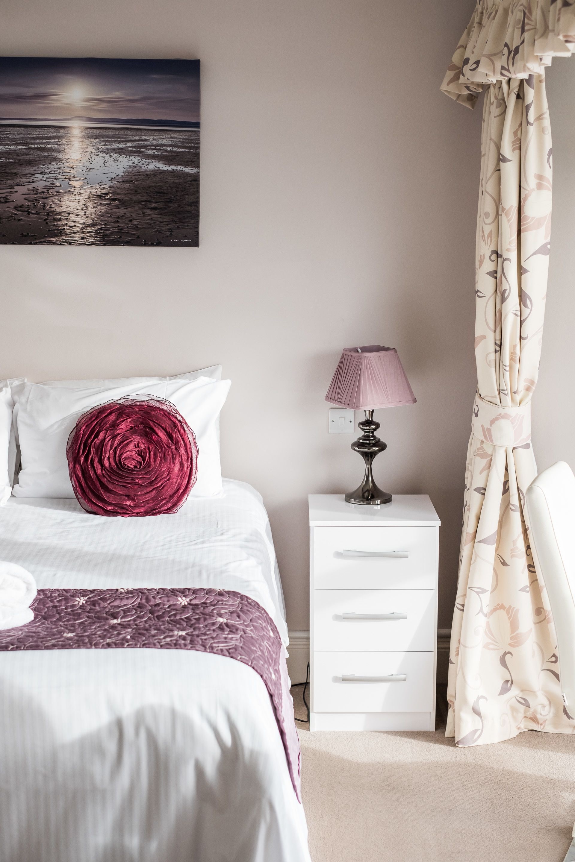 A neatly arranged bedroom with a bed, a bedside table with a lamp, a nightstand, and a curtain.