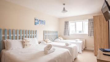 A hotel room with two beds, a wooden headboard, a window with curtains, a flat-screen TV, and a painting on the wall.
