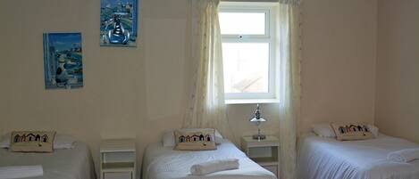 A hotel room with two single beds, a nightstand with a lamp, a window with curtains, and two wall art pieces.