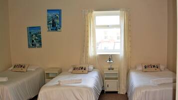 Habitación de hotel con dos camas individuales, una mesita de noche con lámpara y dos cuadros colgados en la pared.