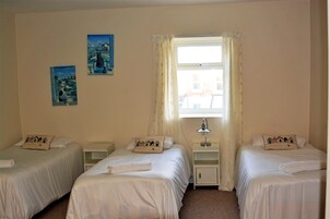 Habitación de hotel con dos camas individuales, una mesita de noche con lámpara y dos cuadros colgados en la pared.