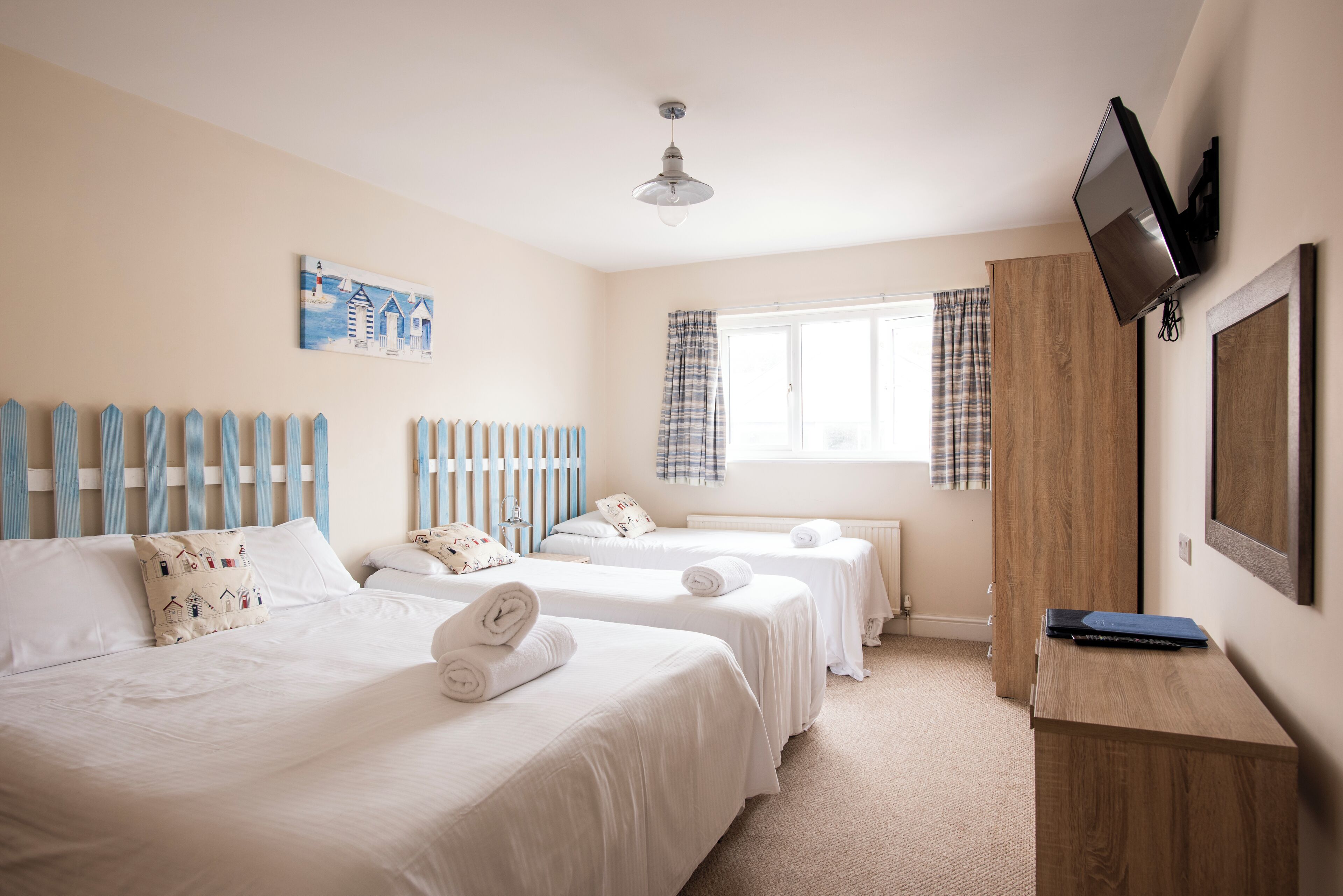 Una habitación de hotel con dos camas, un armario de madera, un televisor y una ventana con cortinas.