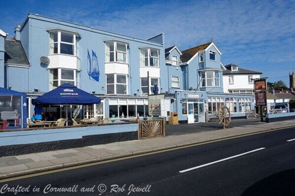 Un bâtiment situé sur la côte, doté de nombreuses fenêtres et d’une façade bleue, qui ressemble probablement à un hôtel ou à un restaurant.