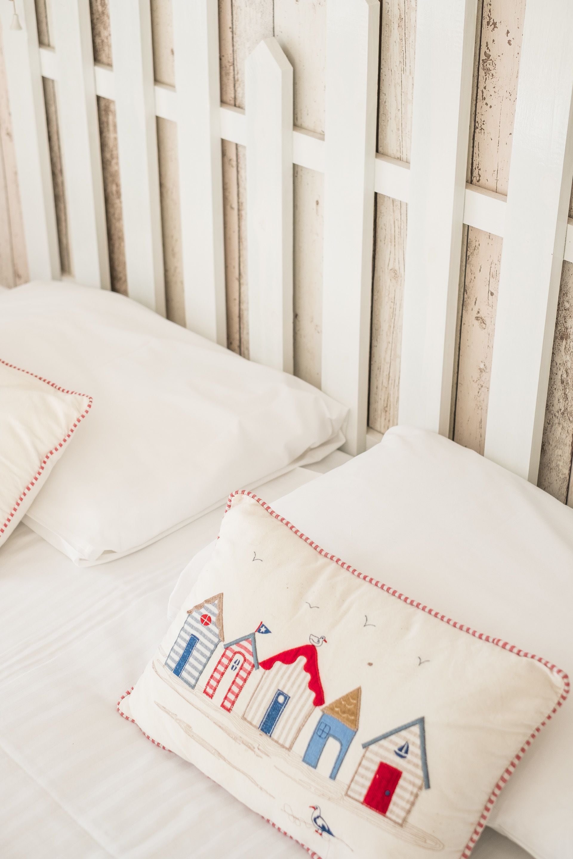 A white bed with a wooden headboard and decorative pillows with a nautical theme.