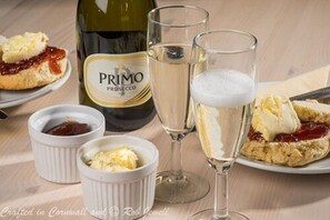 Une table dressée avec une bouteille de Primo Rosé, deux coupes de champagne et une assiette de scones accompagnés de confiture et de beurre.
