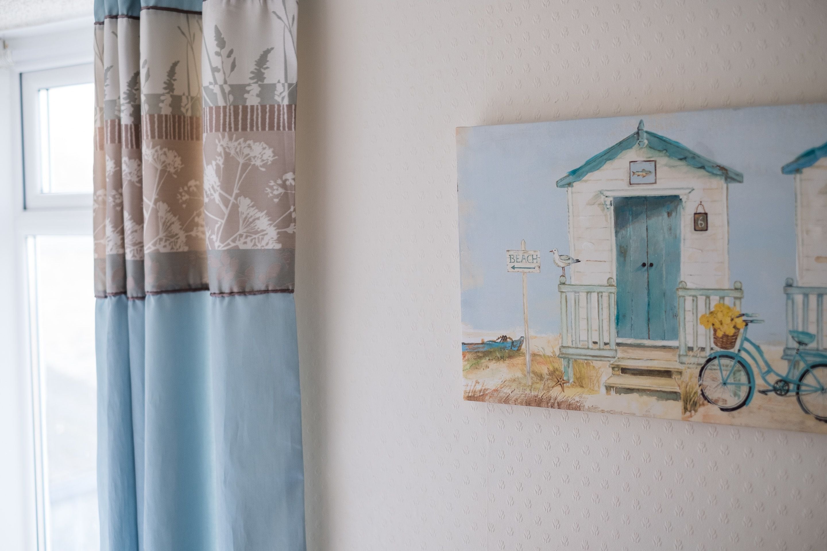 Quarto com pintura de uma casa de praia, uma bicicleta e um letreiro que diz 'BEACH'.
