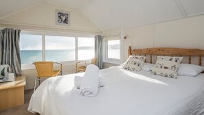 A hotel room with a large bed, a wooden headboard, a chair, a desk with a kettle, and a view of the sea through large windows. - The Lugger Inn (Penzance)