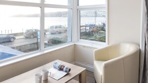 A room with a large window, a white chair, a wooden table with two white mugs, and a magazine. - The Lugger Inn (Penzance)