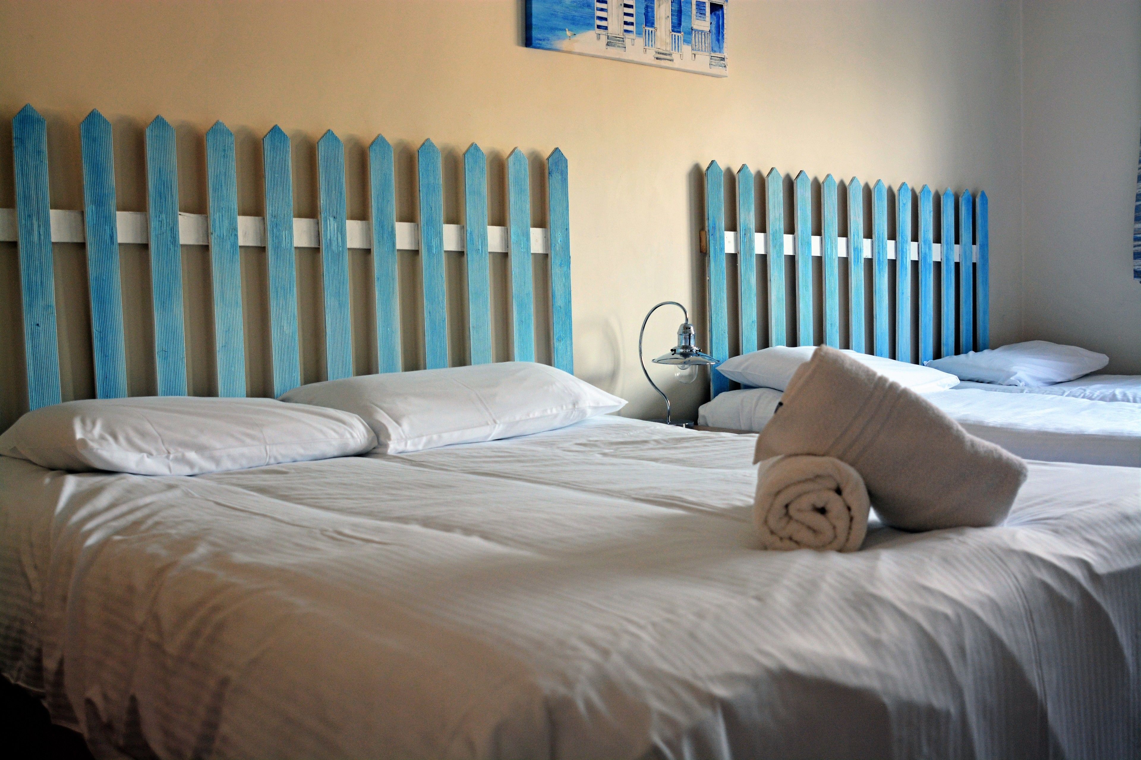 A hotel room with two beds, white bedding, and a blue-painted headboard.