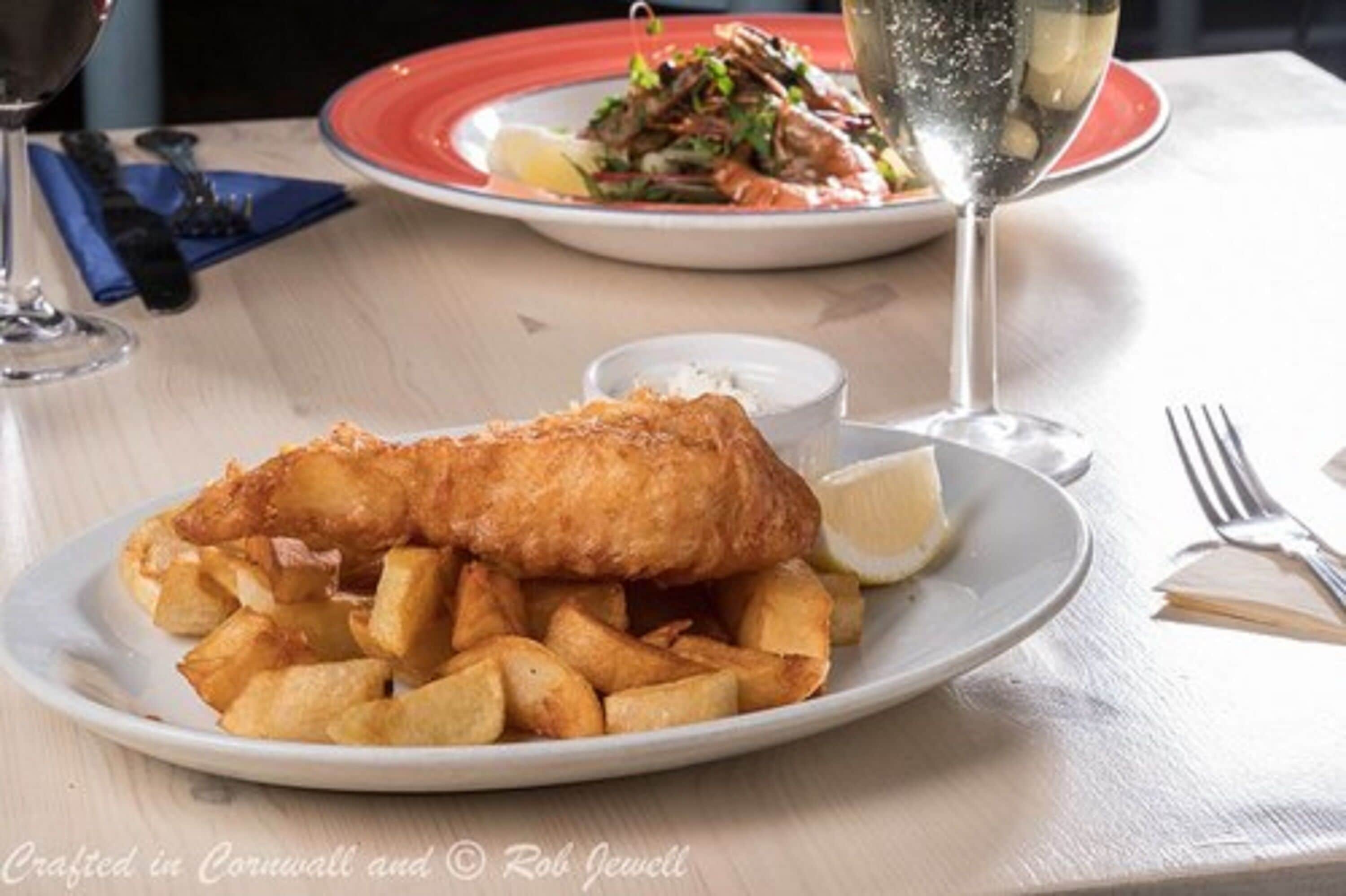 Un plato de pescado con papas fritas y una cerveza sobre una mesa.