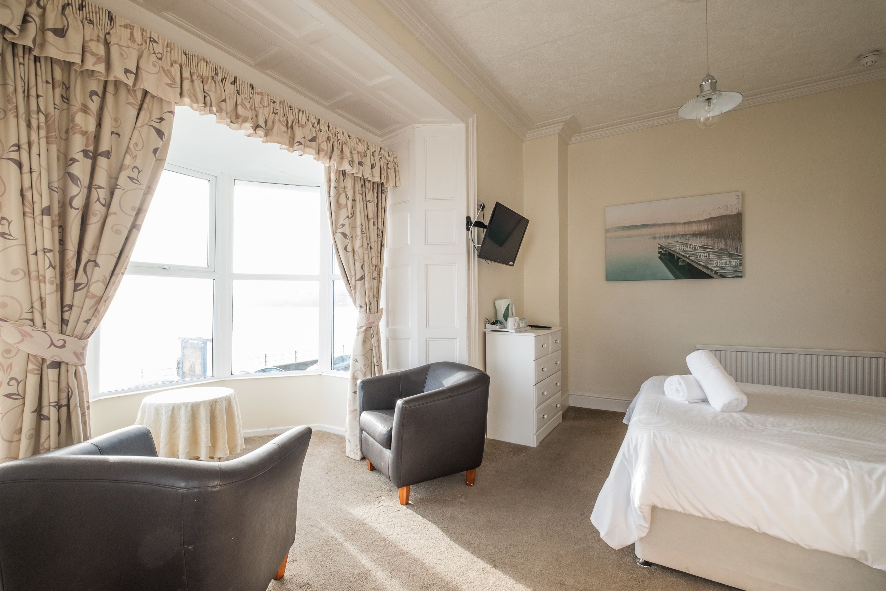 A hotel room with a bed, a chair, a desk, a TV, and a window with curtains.